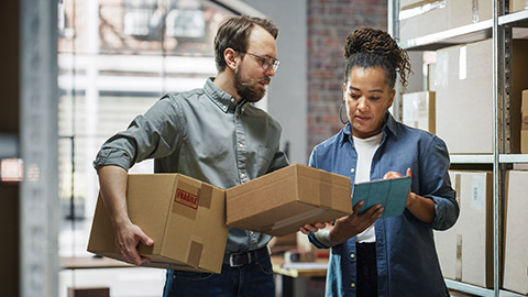 female inventory manager using tablet computer, talking to a worker holding two cardboard packages