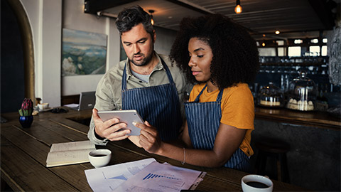 Concerned male and female coffee shop owners scrolling on tablet in rustic coffee shop.