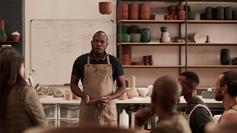 ceramist wearing an apron talking with a diverse group of coworkers