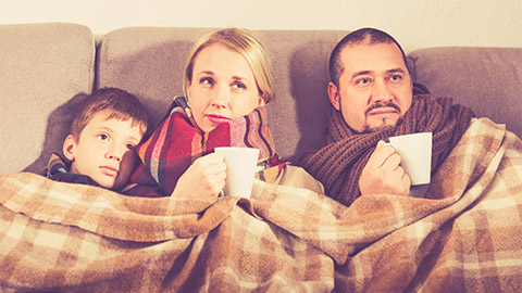 A family huddling together for warmth under a blanket, on their sofa