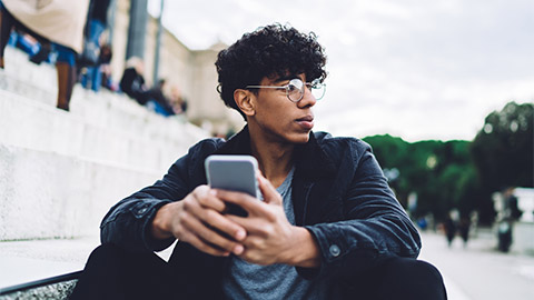 A young person looking off into the distance while holding their mobile phone