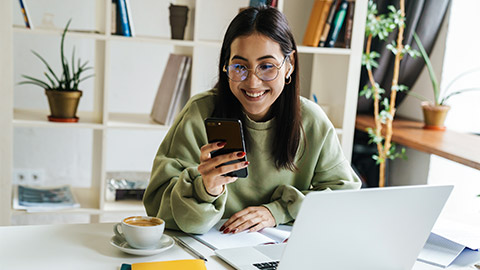 A young person in front of their laptop and on their phone