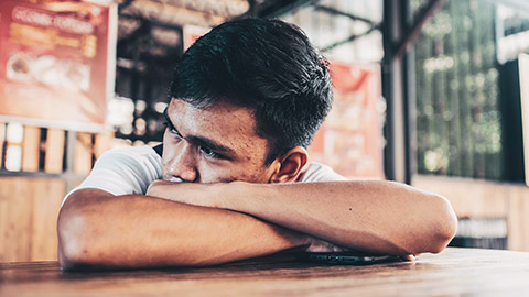 A serious teenager looking troubled while sitting at a table