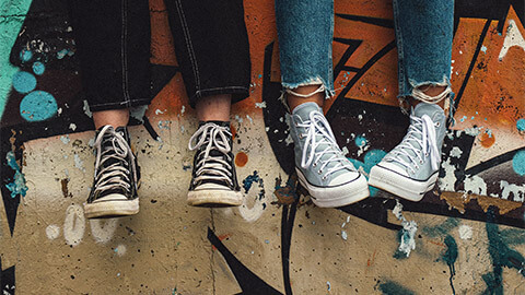 Two teenagers seated on a concrete wall covered in street art