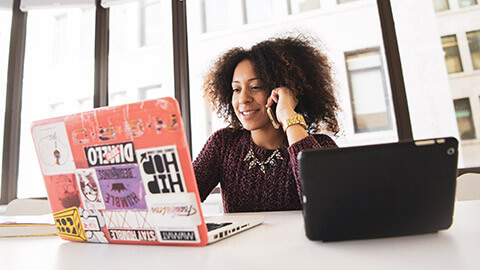 A youth worker sitting at a table, looking at a laptop while talking on a phone