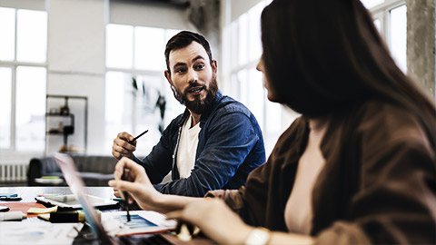 coworkers sitting at wooden table with laptop and papers while discussing data details