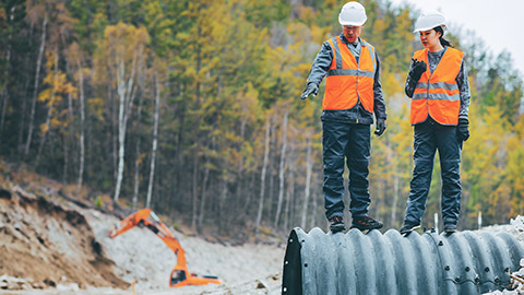 2 workers standing on water draininage pipe on building site