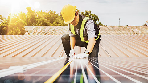 A low angle view of a man installing a solar panel on a roof