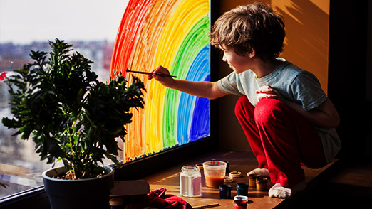 a child painting the window with rainbow colors