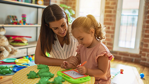 teacher and blond student toddler girl drawing using digital board at kindergarten