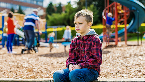 boy sitting at the park, scared and apprehensive about playing with the other children