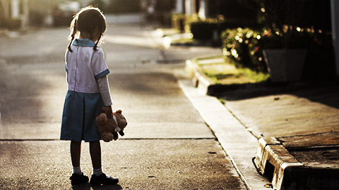 a sad shild on the street holding a teddy bear