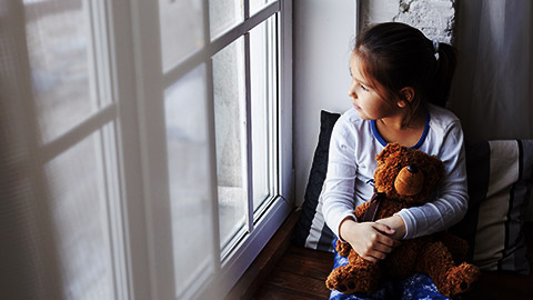 a child with a teddy bear looking out the window