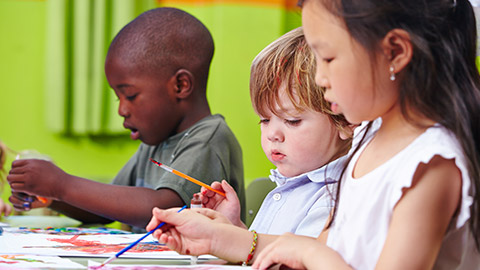 Different children concentrate together painting pictures in kindergarten