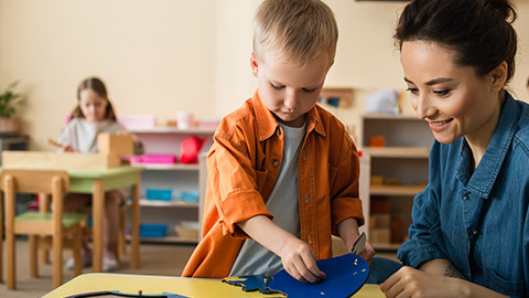 boy combining earth map puzzle near smiling teacher and girl on blurred background