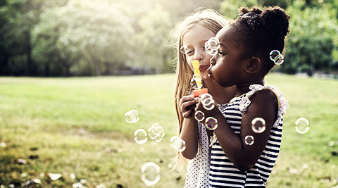 Two kids of different races playing and blowing bubbles