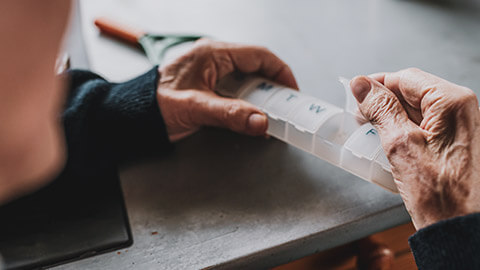 A close view of an elderly person opening a pill dispenser