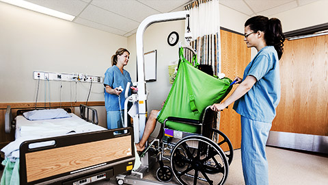 A couple of nurses using a sling to help a patient on the bed