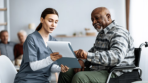 oung woman nurse helping senior black man in wheelchair with questionnaire