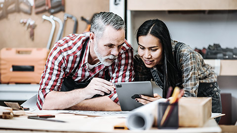 A senior man assisted in technology by a young woman