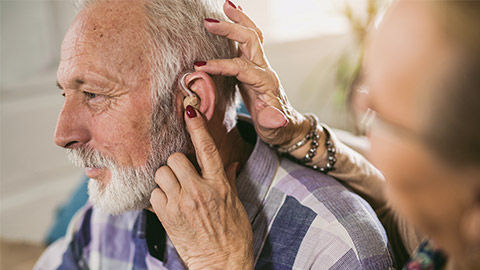 an old man with hearing problem and being assisted by his wife