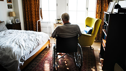 A rear wide shot of an elderly person in a wheelchair in a lonely room