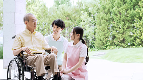 two healthworkers assisting an elderly man on chair