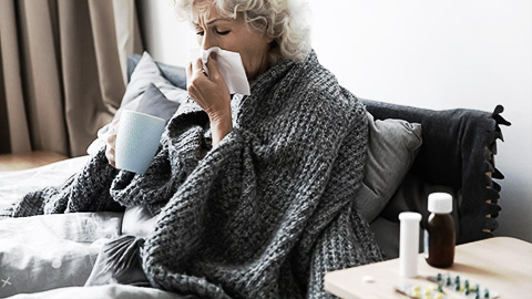 An elderly sneezing while on a bed