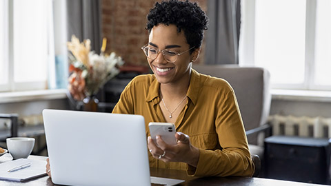 woman sit at workplace desk holds cellphone staring at laptop