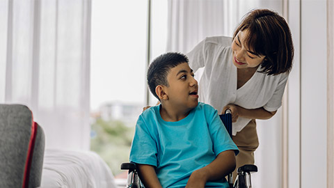 carer helping look at disabled child sitting in wheelchair