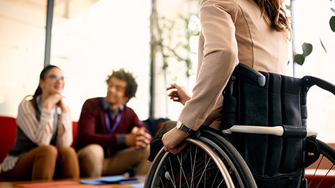 Unrecognizable businesswoman in wheelchair communicating with her coworker in the office