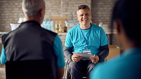 Happy volunteer with disability giving instructions to his team while organizing donation at community center.