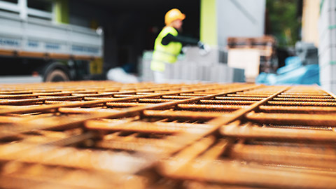 Close view of stack of rebar with person in high-vis is the background