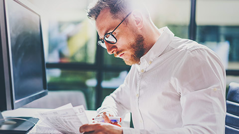 Close view of young business professional sitting at a desk reading paperwork with a computer in the background