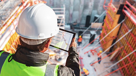 Over the shoulder view of construction manager on site looking at gantt chart on tablet device