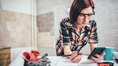 A tradesperson looking at their phone while consulting the plans on a desk