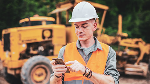 A worker on a worksite checking his phone for work-related news