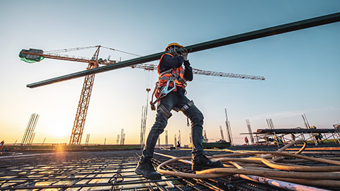 A worker on a construction site carrying a large steel beam