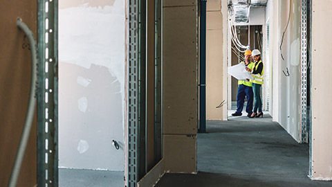 2 construction workers consulting plans while standing in the interior of a new-build house