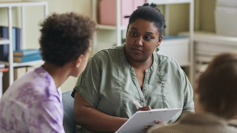 African American psychologist listening to teenage boy and making notes, she working with difficult teenagers at class