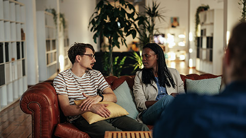 Biracial couple sitting on couch in psychotherapist office and trying to solve problems, save relationship