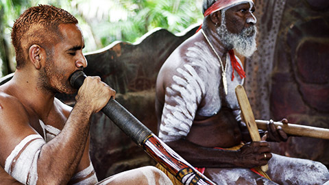 Australian Aboriginal men play Aboriginal music on didgeridoo and wooden instrument during Aboriginal culture show in Queensland, Australia.