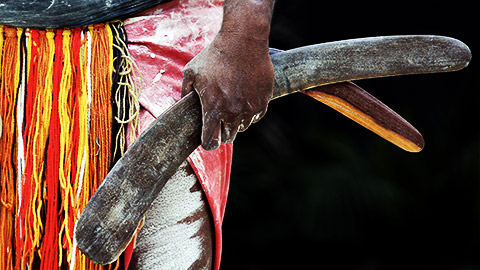 An indegenous person holding a pair of boomerangs