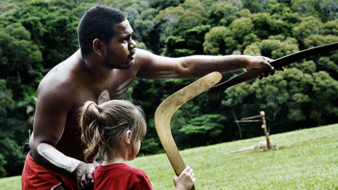 An aborigine teach a white child how to throw a boomerang