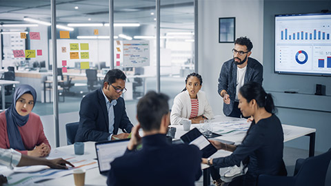 Diverse Modern Office: Businessman Leads Business Meeting with Managers, Talks, uses Presentation TV with Statistics, Infographics.