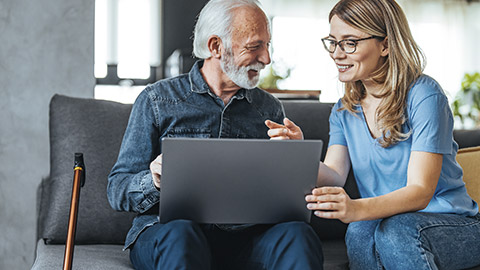 carer teaching elder man on computer