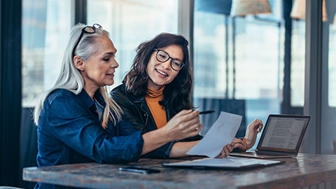 Two women analyzing documents while sitting on a table in office