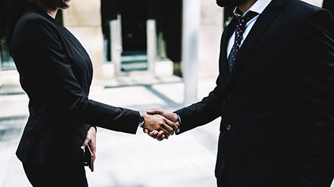 two people  in strict formal black suits shaking hands greeting each other in street