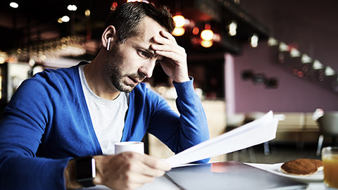 A person in a cafe frustrated while reading a financial papers