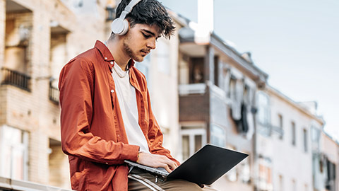 Man studying with computer outside the campus with headphone